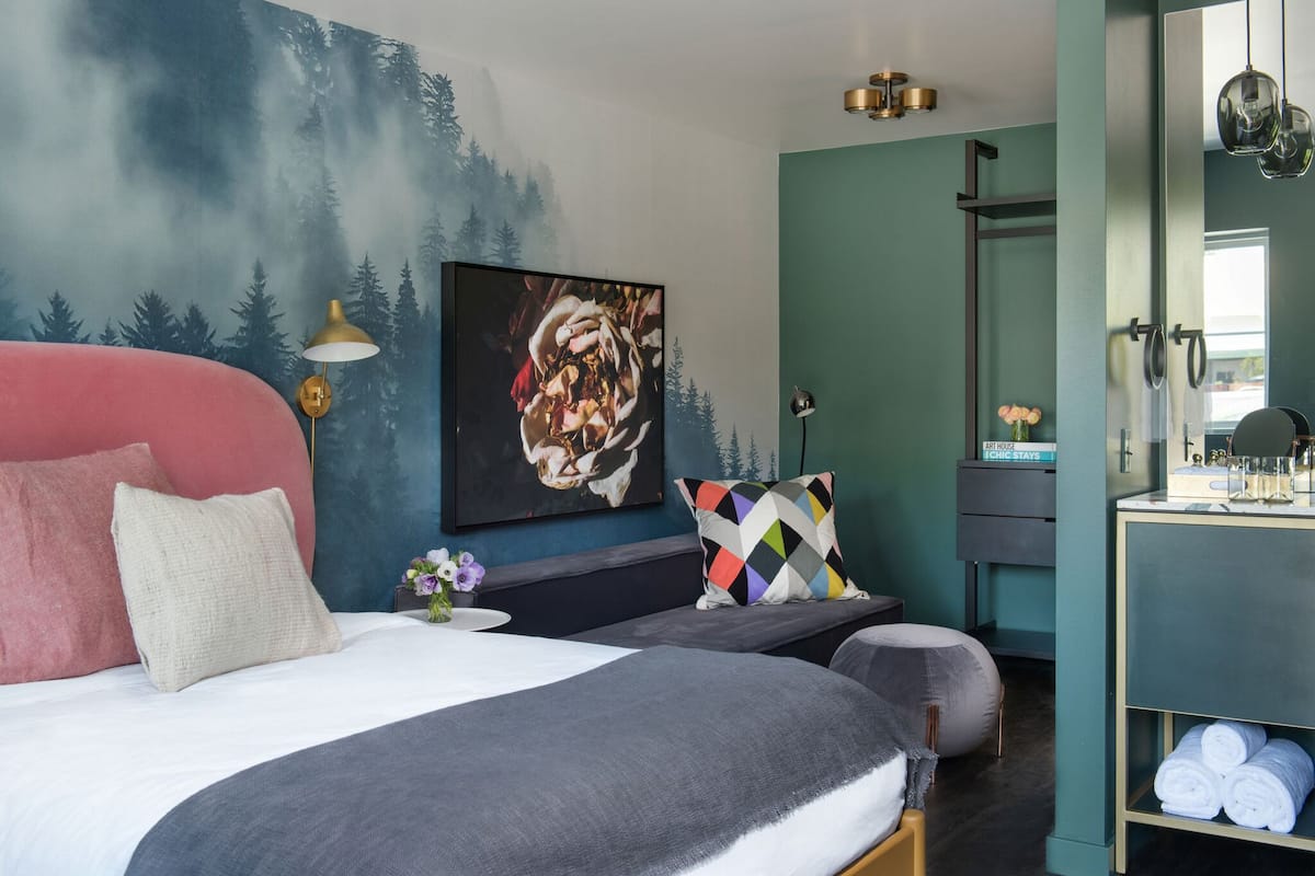 A modern bedroom with a bed, a bench, a painting, and a vanity with towels.