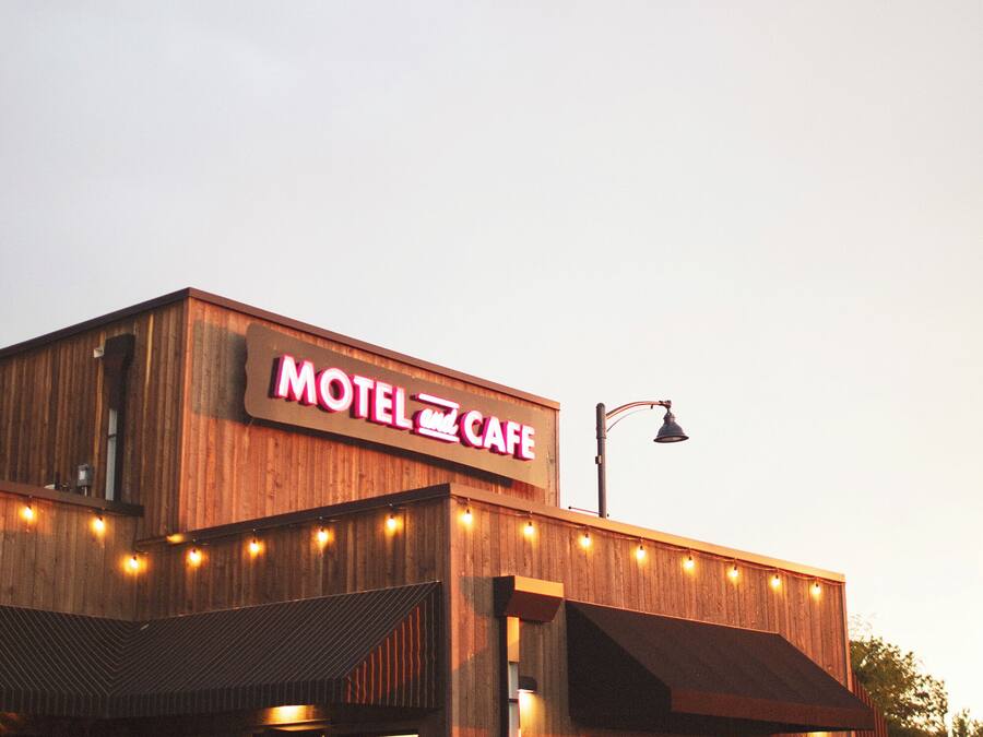 A motel with a prominent sign, a covered outdoor seating area, and a street view.