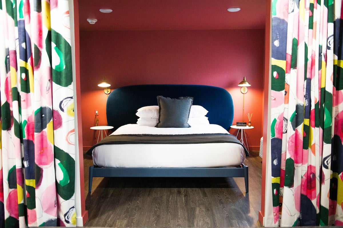 A modern bedroom with a large bed, two bedside tables, and a red accent wall.