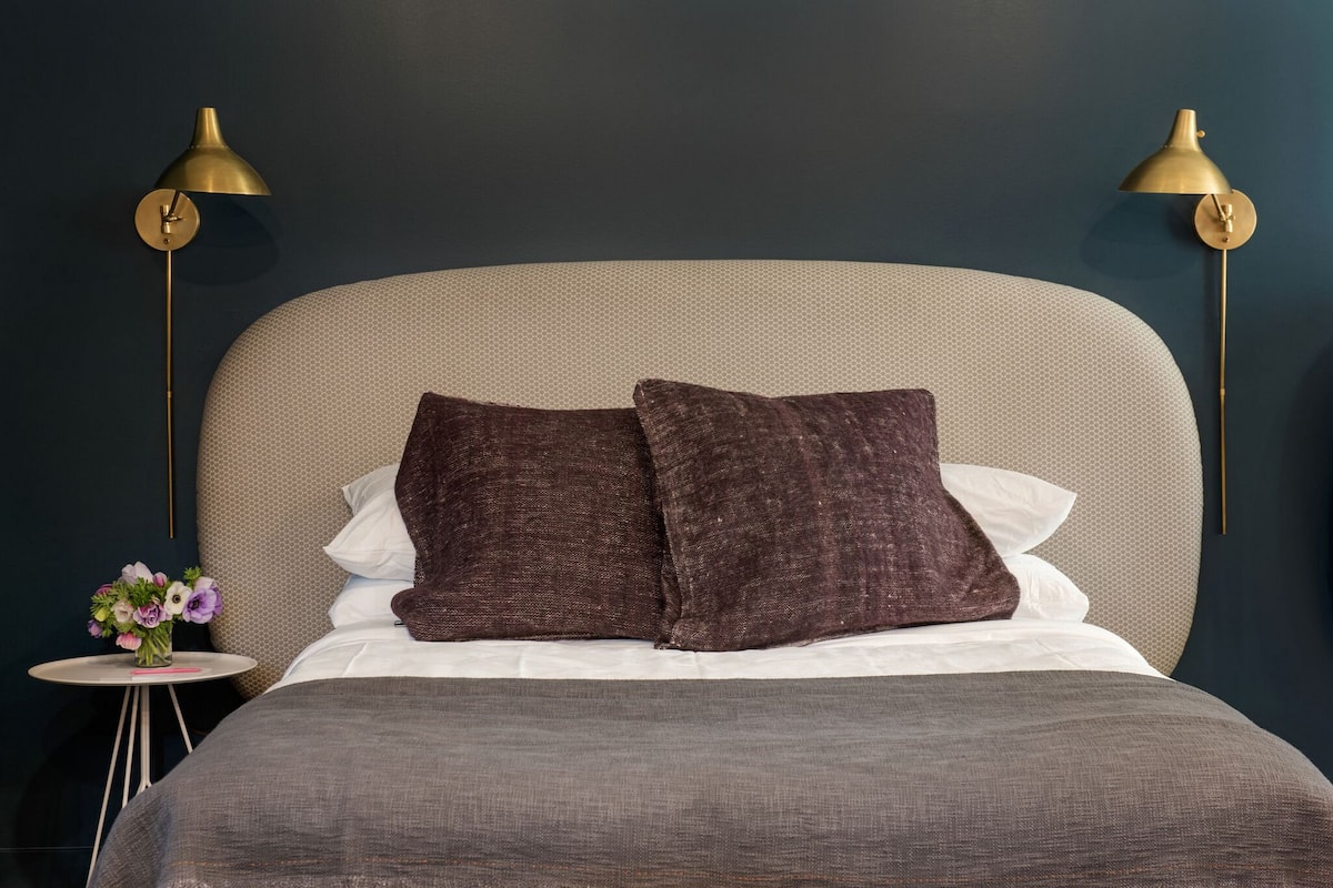 A neatly made bed with a grey bedspread and two brown pillows, flanked by two gold lamps on either side.