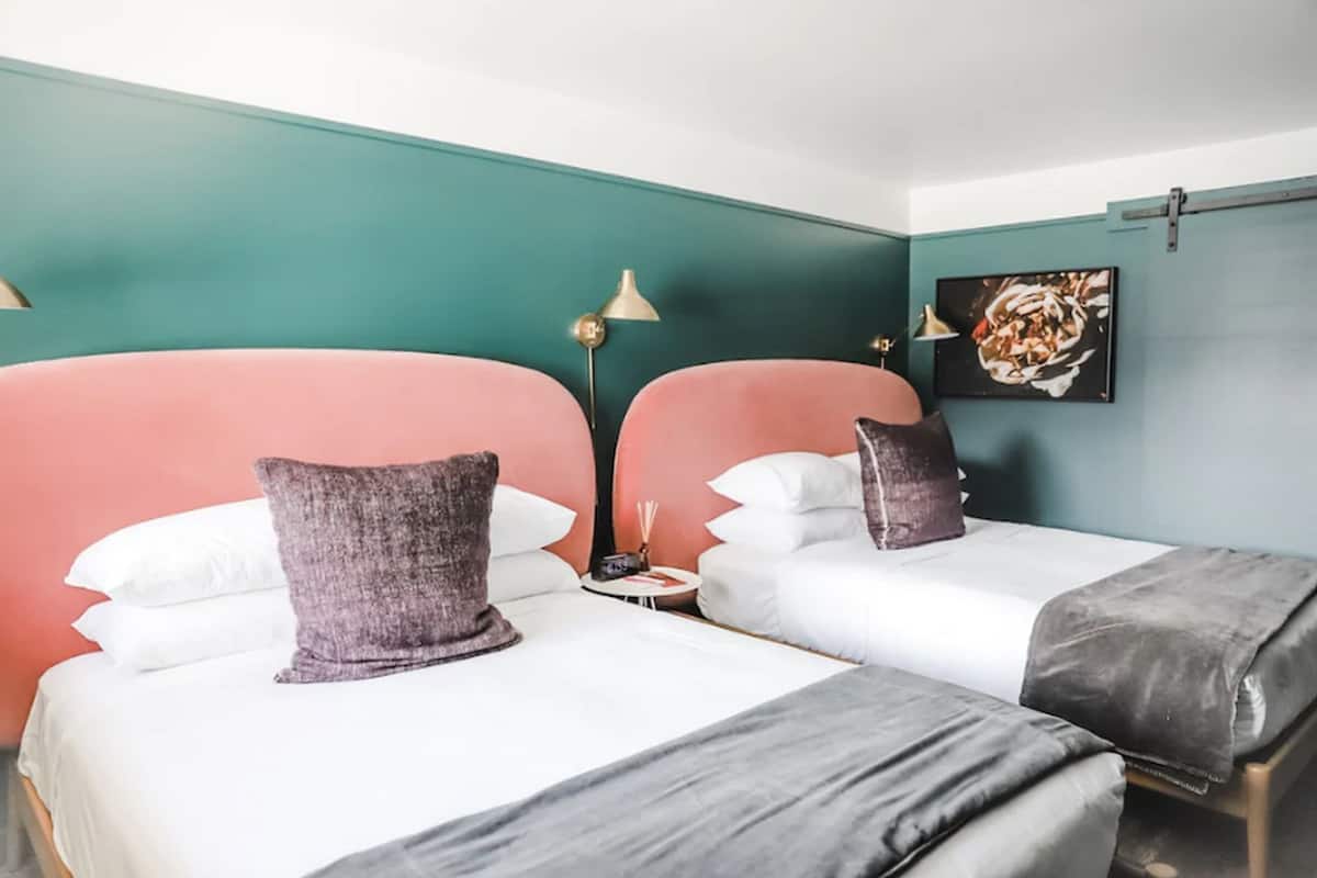 A hotel room with two beds, teal walls, and a small table with a lamp.
