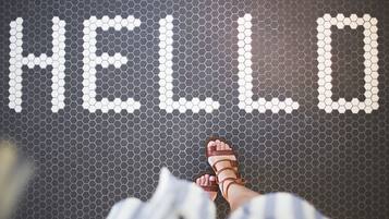 A person's feet standing on a hexagonal tile floor with the word "HELLO" spelled out in white tiles.