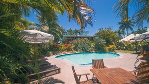 A pool area with lounge chairs and umbrellas, surrounded by tropical plants and a building in the background. - Arcadia Retreat Rarotonga (Rarotonga)