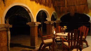 An outdoor seating area with wooden chairs and a table, surrounded by stone pillars and a thatched roof structure. - Hacienda Antigua Villa (Mexico City)