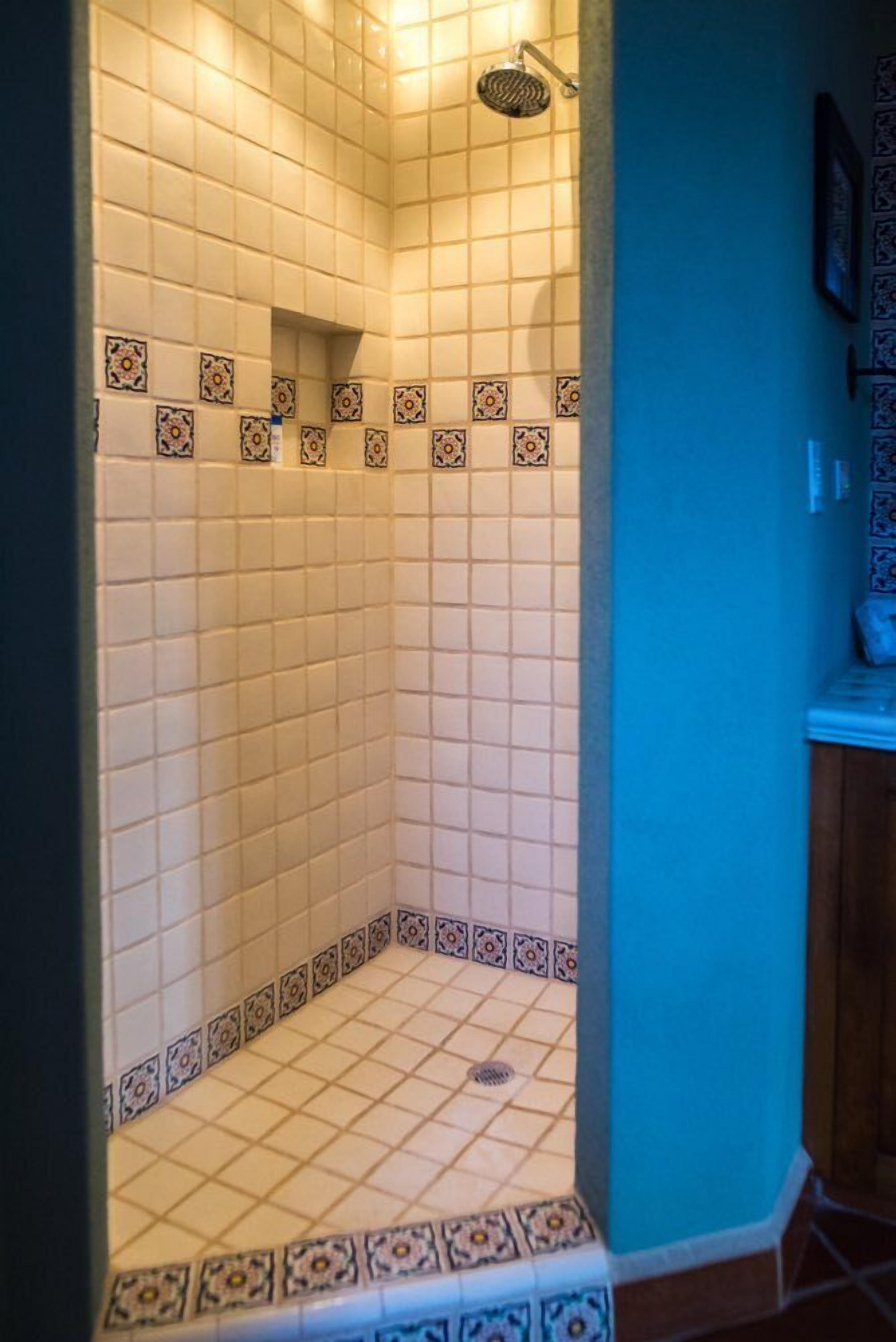 Ducha con azulejos blancos y un borde decorativo.