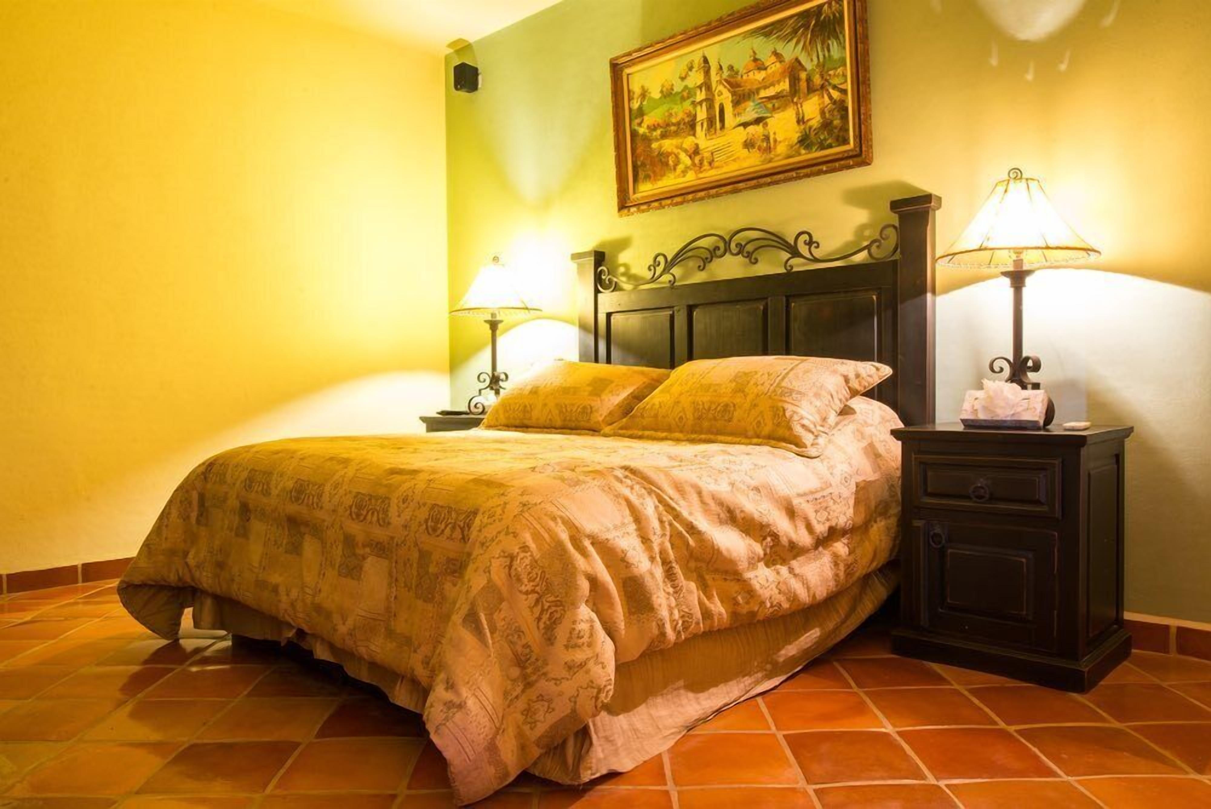 Une chambre à coucher avec un lit, deux tables de chevet, une commode, un tableau au mur et un sol carrelé.