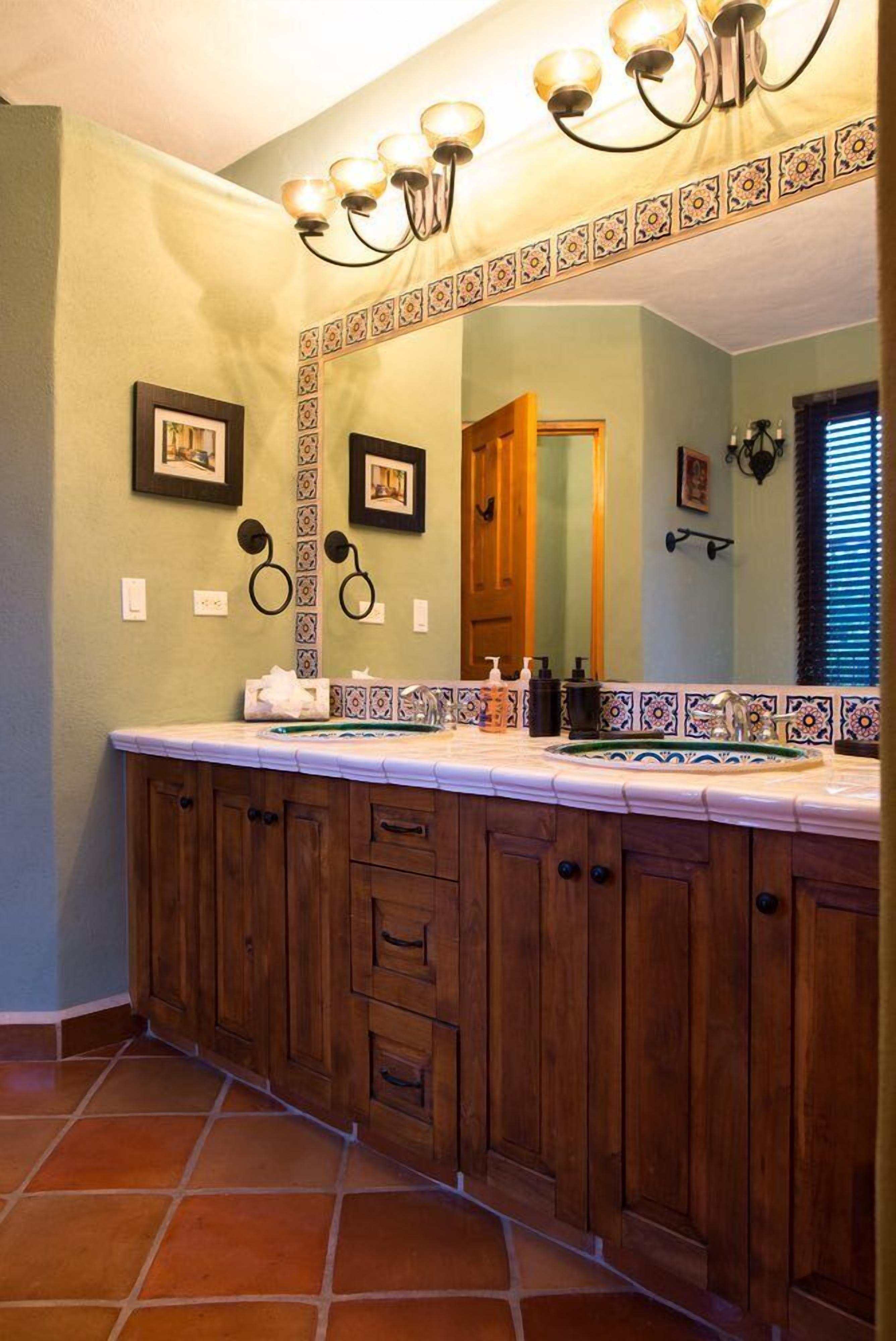 Ein Badezimmer mit einem großen Holzbadschrank, einem Spiegel mit dekorativen Kacheln und einem Kronleuchter.