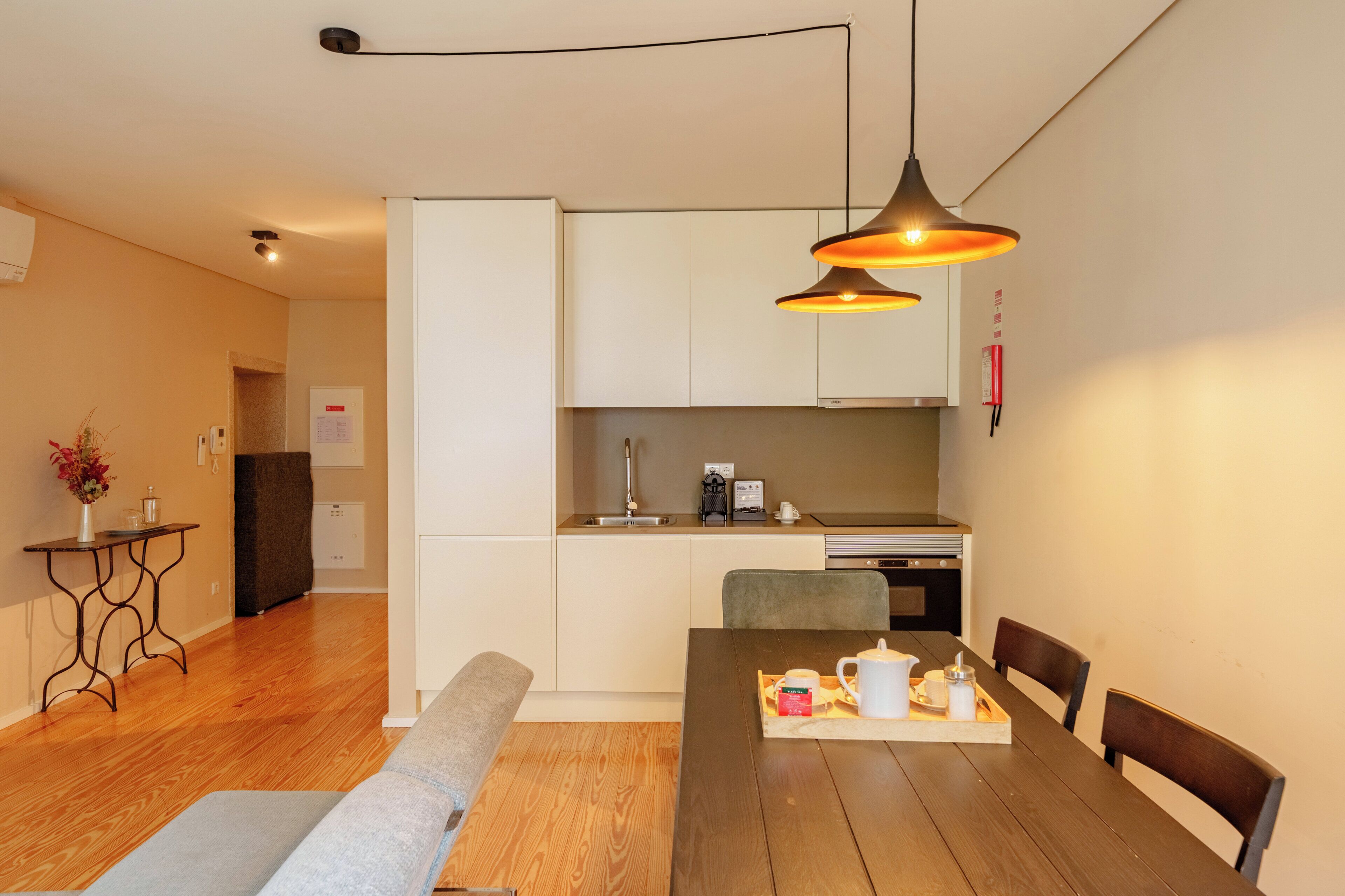 Une cuisine moderne avec des meubles blancs, une table à manger avec des chaises et des luminaires suspendus.