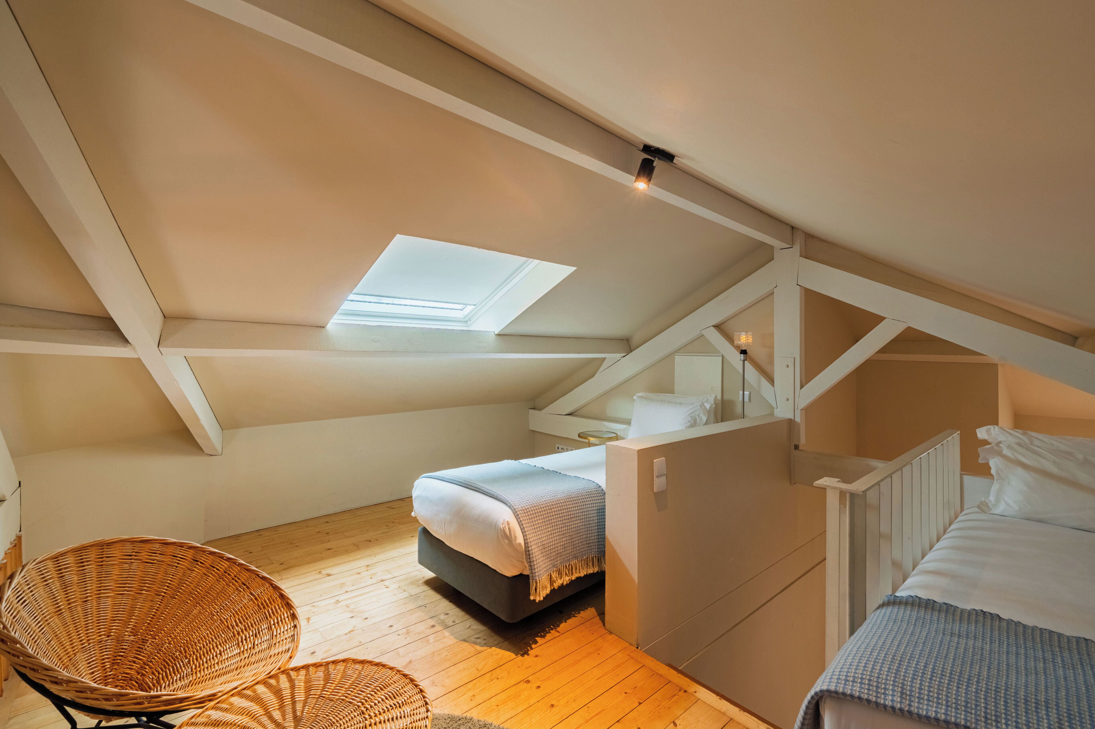 An attic bedroom with a skylight, a bed, a chair, and a small table.