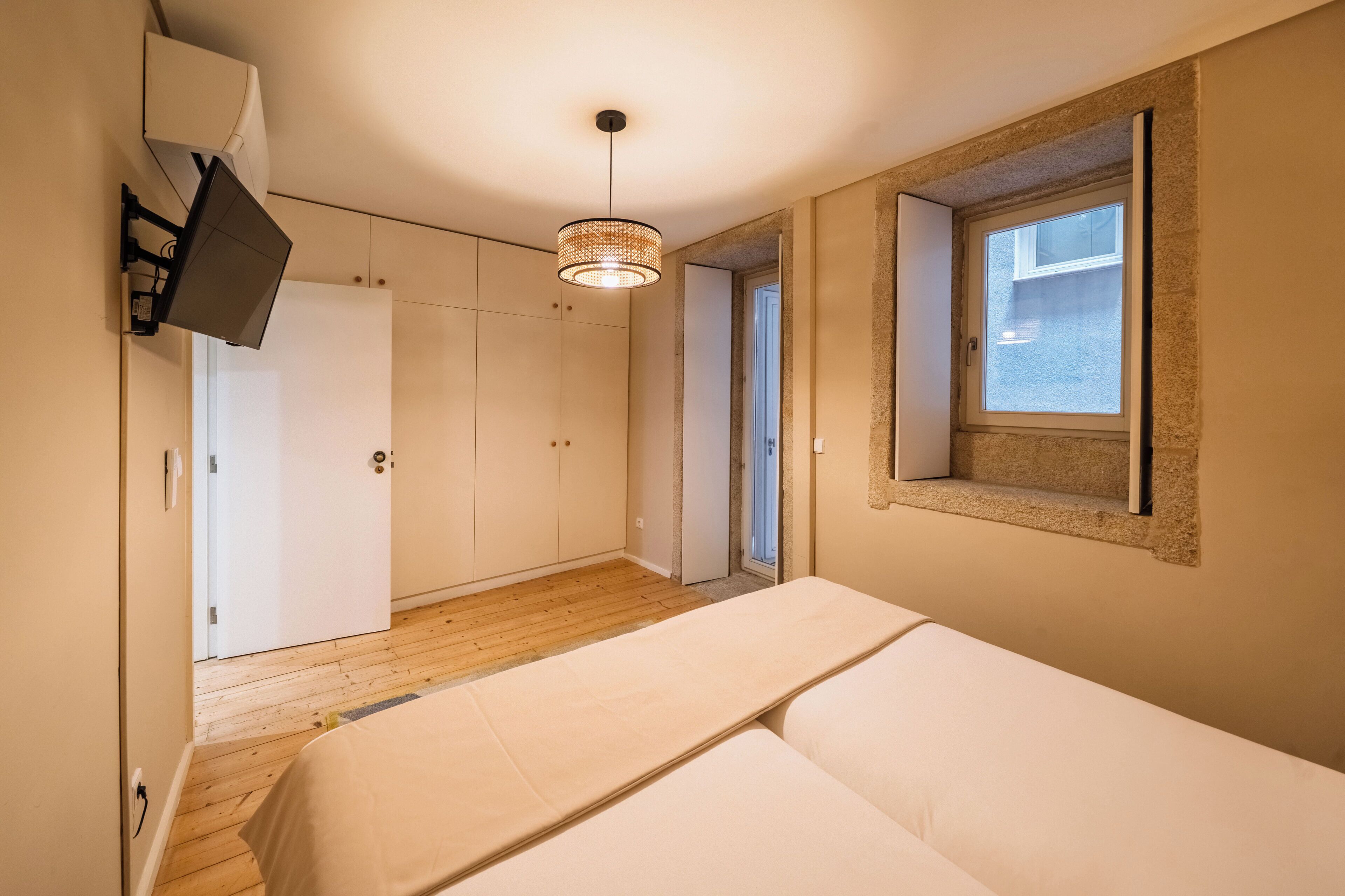 A bedroom with a bed, a wardrobe, a hanging light fixture, and a window.