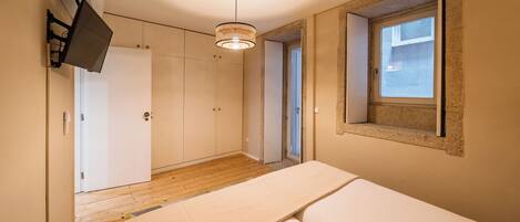 A bedroom with a bed, a wardrobe, a hanging light fixture, and a window.