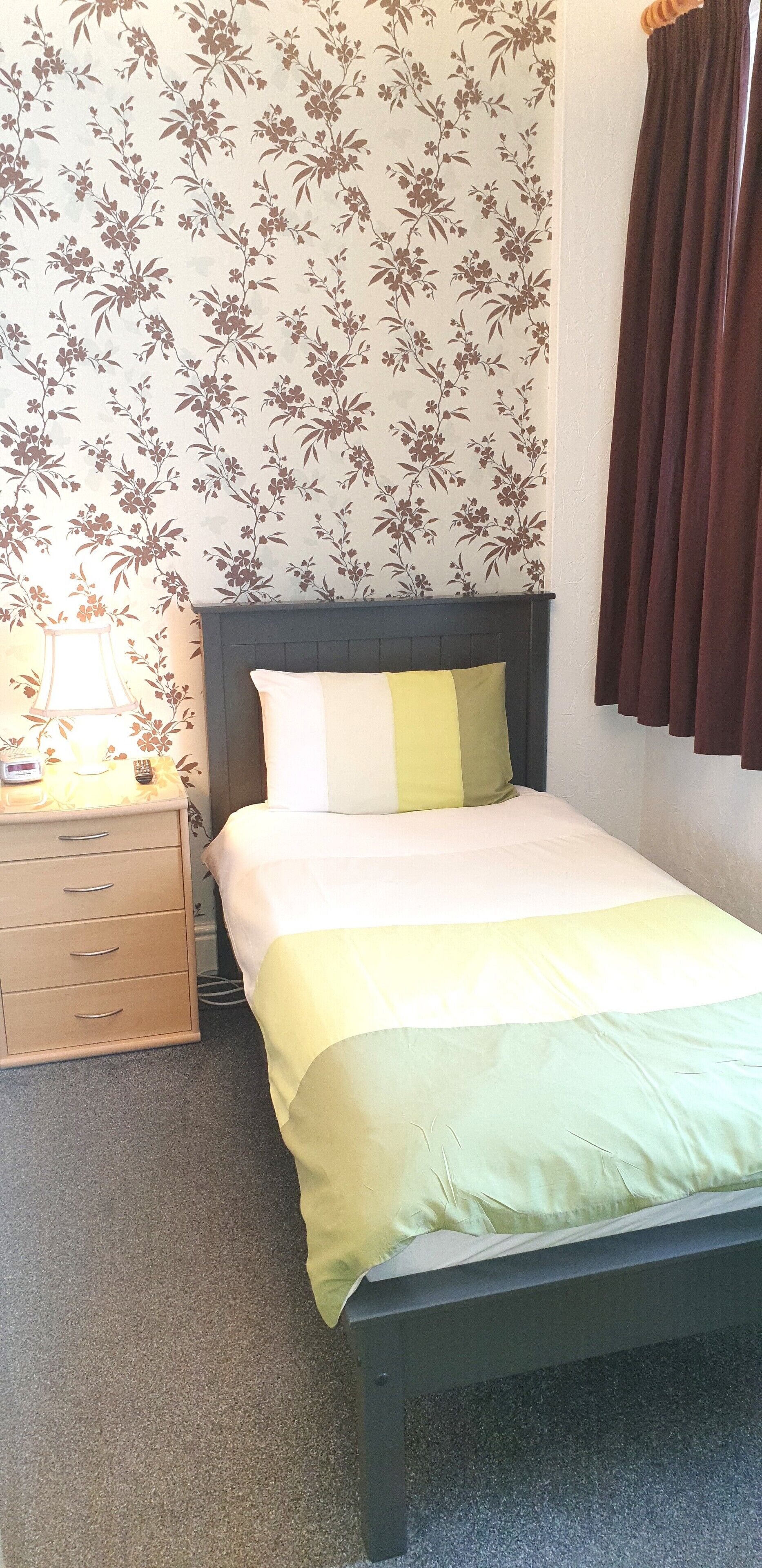 A bedroom with a bed, a nightstand, a lamp, and a floral wallpaper.
