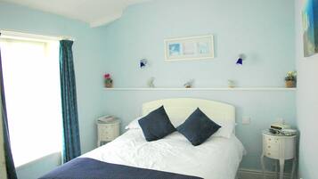 A bedroom with a bed, a nightstand, a shelf with decorative items, and a window with curtains.