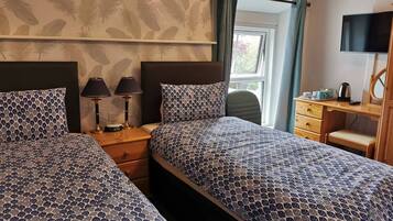 Hotelkamer met twee bedden, een bureau, een stoel, een televisie en een raam met gordijnen.