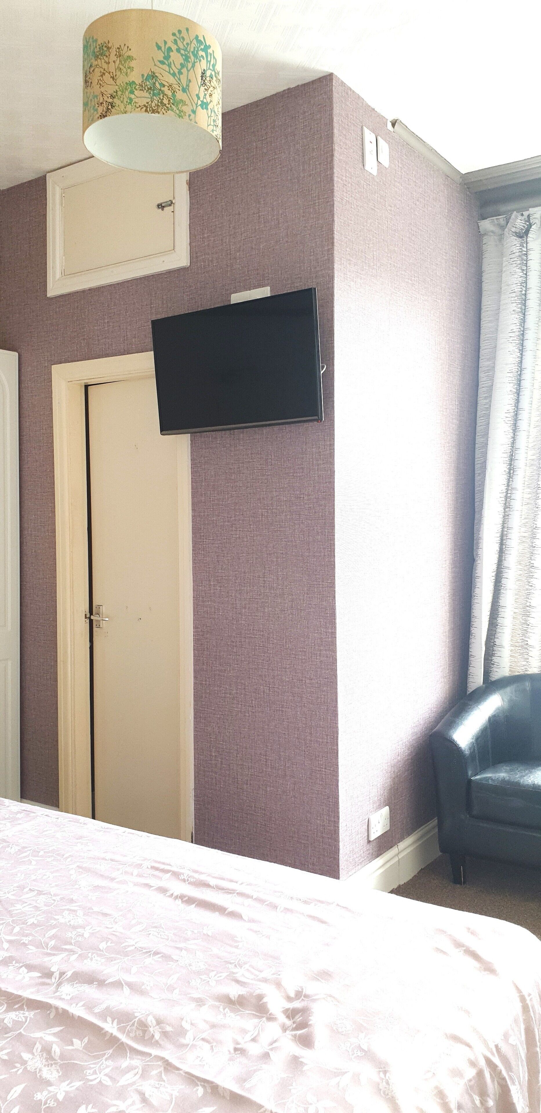 A bedroom with a bed, a television mounted on the wall, a door, and a chair.
