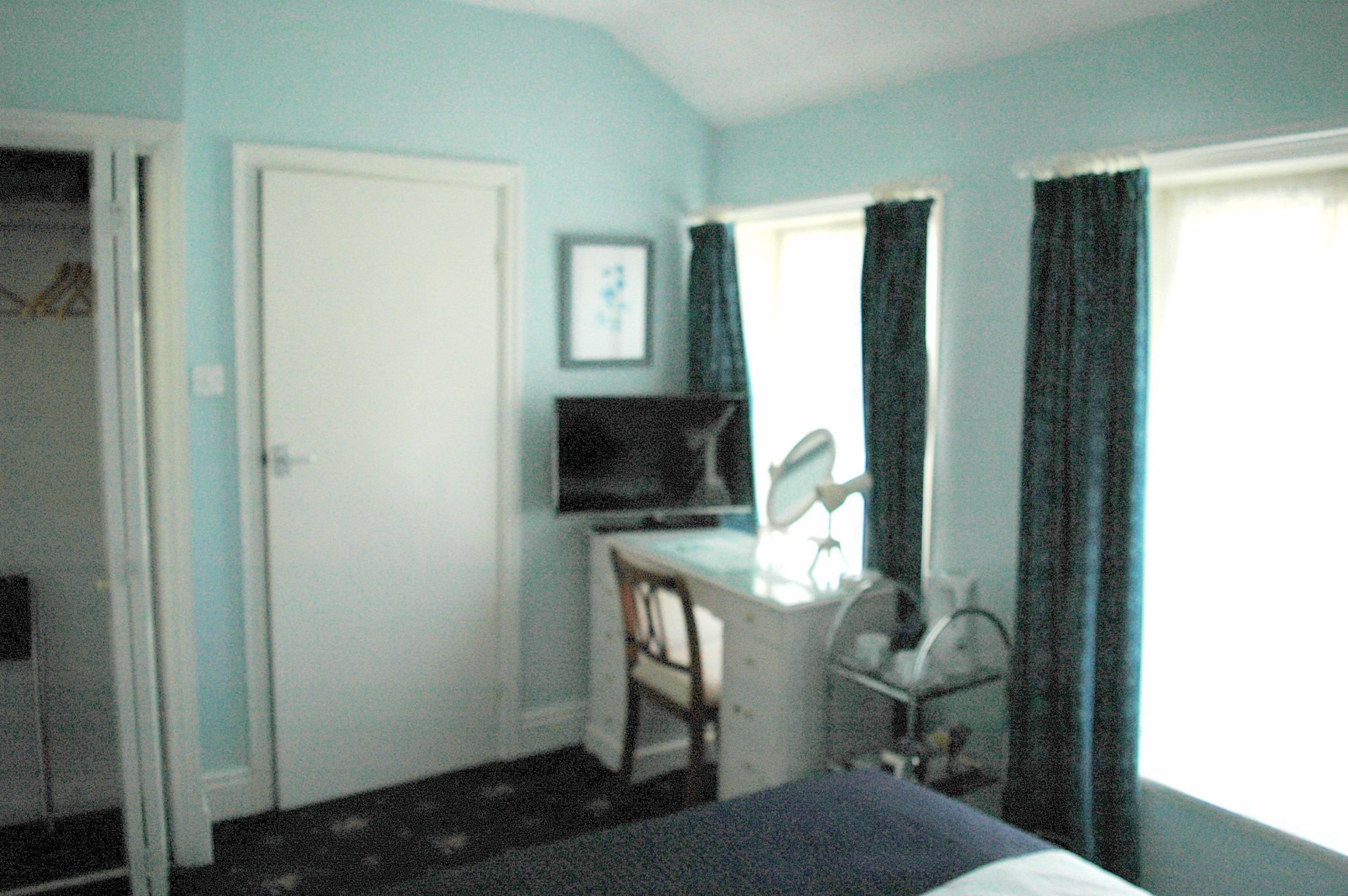 A room with a desk, chair, television, and a window with curtains.