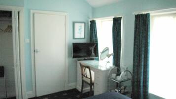 A room with a desk, chair, television, and a window with curtains.
