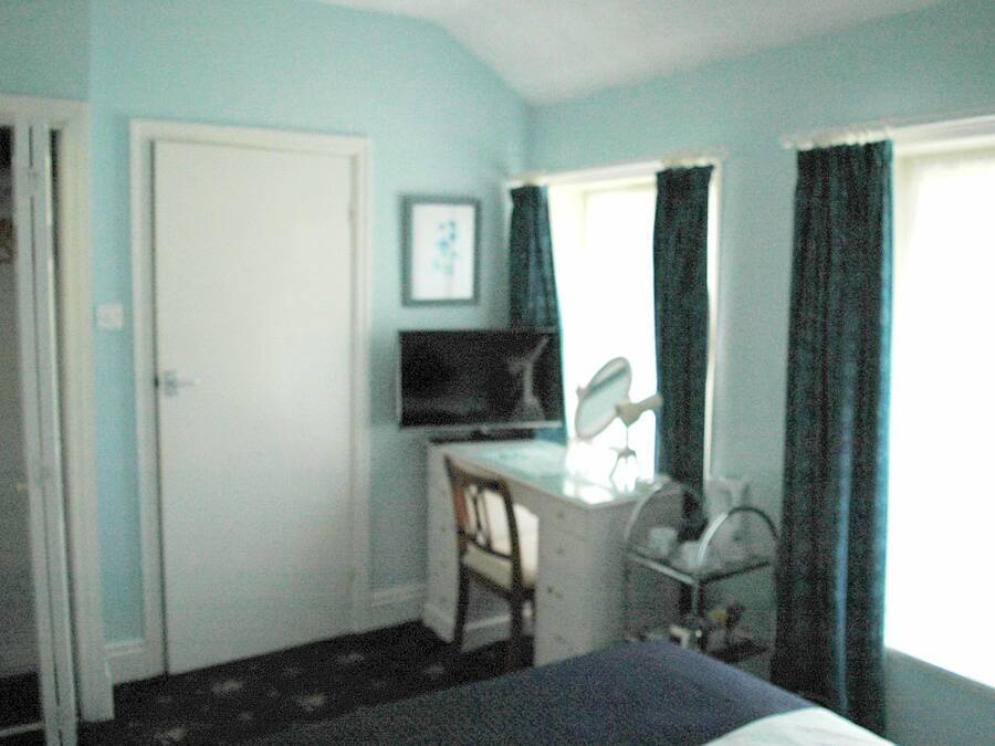 A room with a desk, chair, television, and a window with curtains.
