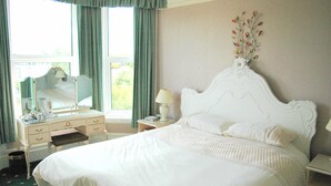 Une chambre à coucher bien rangée, avec un grand lit, une table de chevet avec une lampe, une commode et une fenêtre avec des rideaux.