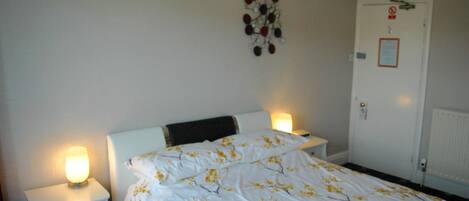 Un dormitorio con una cama, dos mesitas de noche con lámparas, un adorno en la pared y una puerta con un letrero.