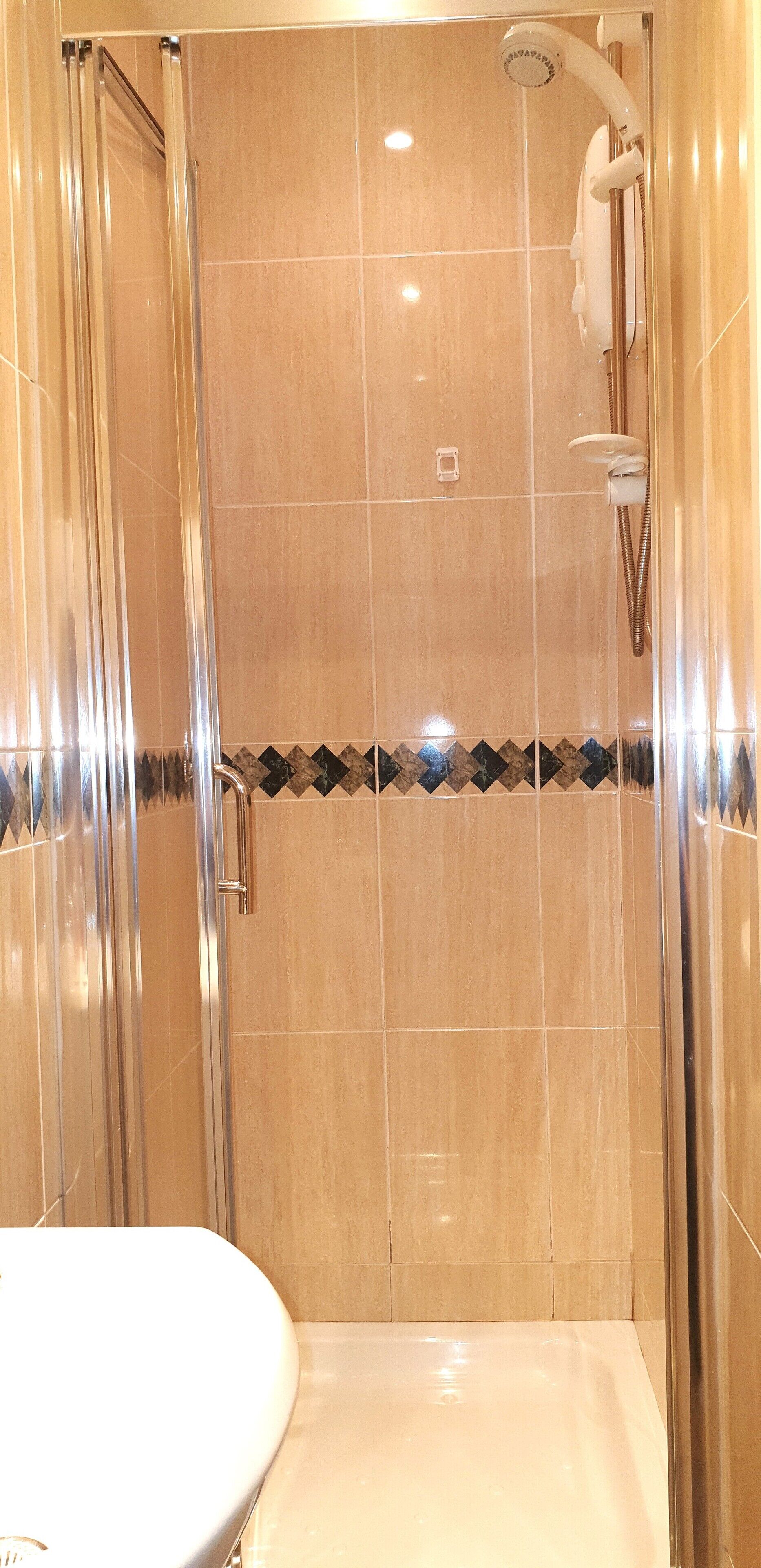 Un baño moderno con ducha envuelta en vidrio, azulejos color crema y un borde decorativo de azulejos.
