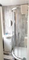 Un baño moderno con ducha envuelta en vidrio, lavabo con espejo y un perchero para toallas.