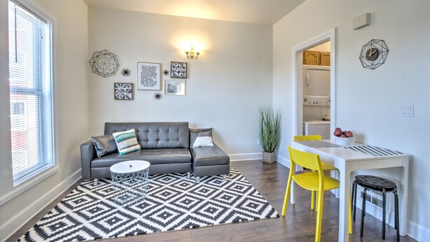 A living room with a gray sectional sofa, a white coffee table, a patterned rug, a yellow chair, and a white dining table with a bowl of fruit. - Capitol Hill Apartments (Seattle)