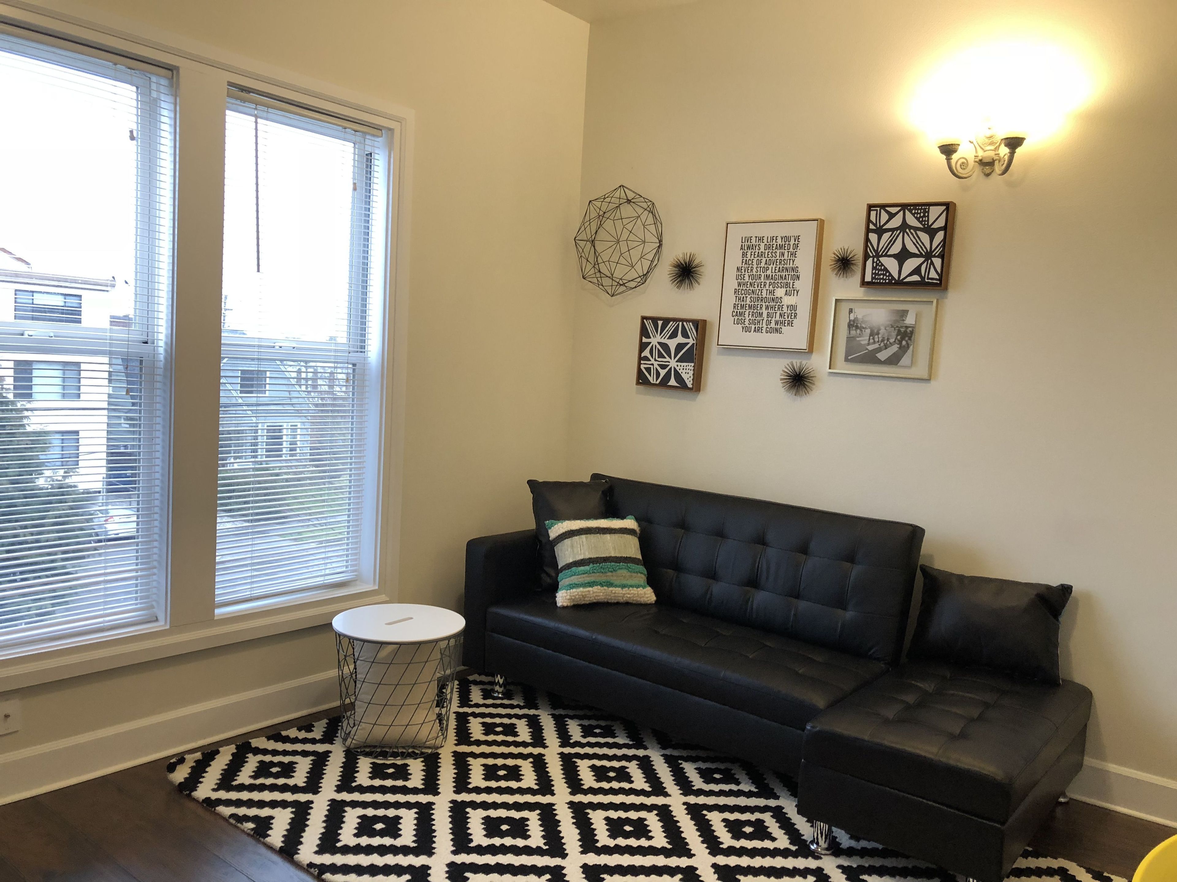 A modern living room with a dark sofa, a patterned rug, and wall art.