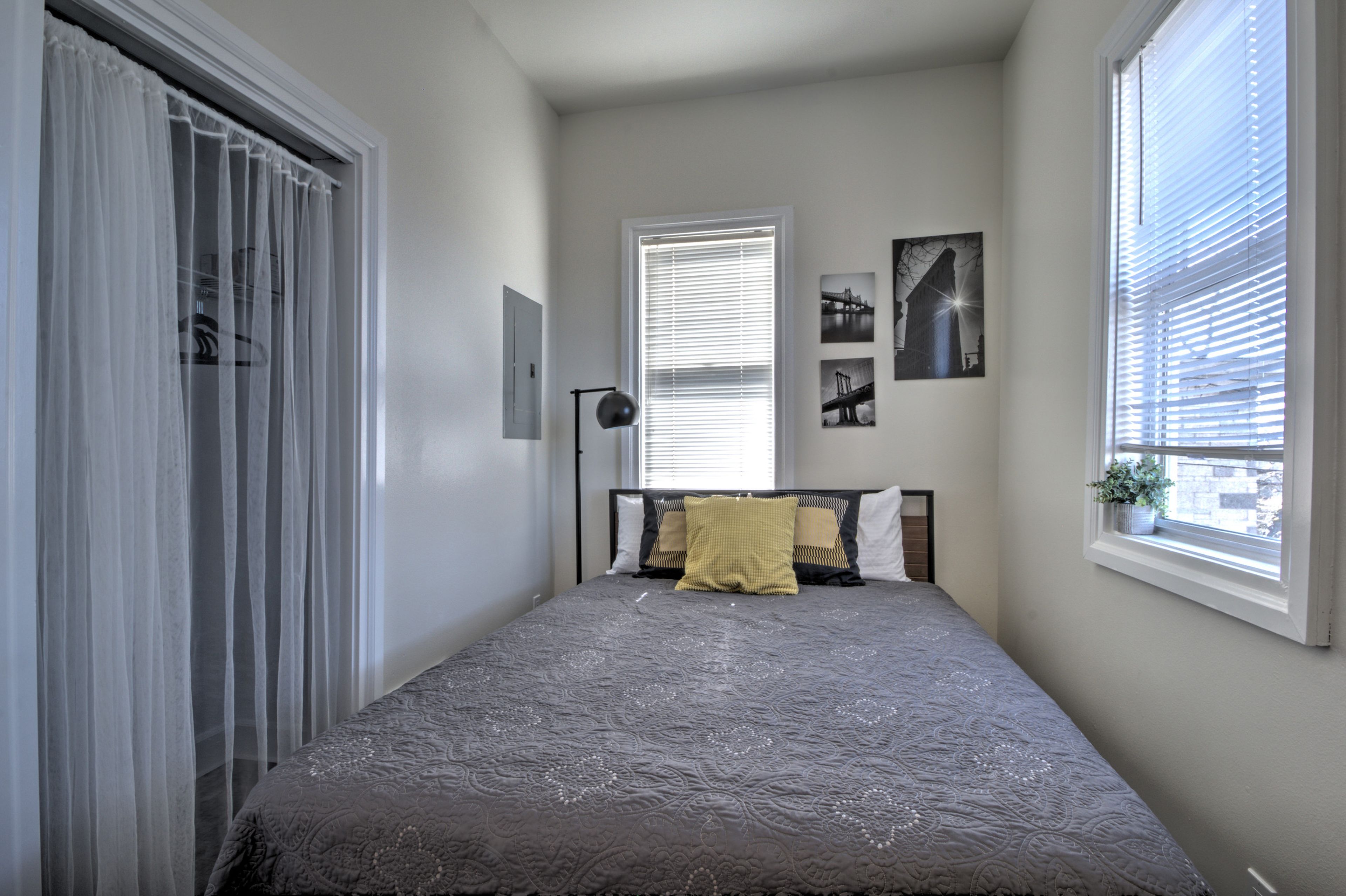 A bedroom with a bed, a window with blinds, a bedside lamp, and a wall-mounted picture.