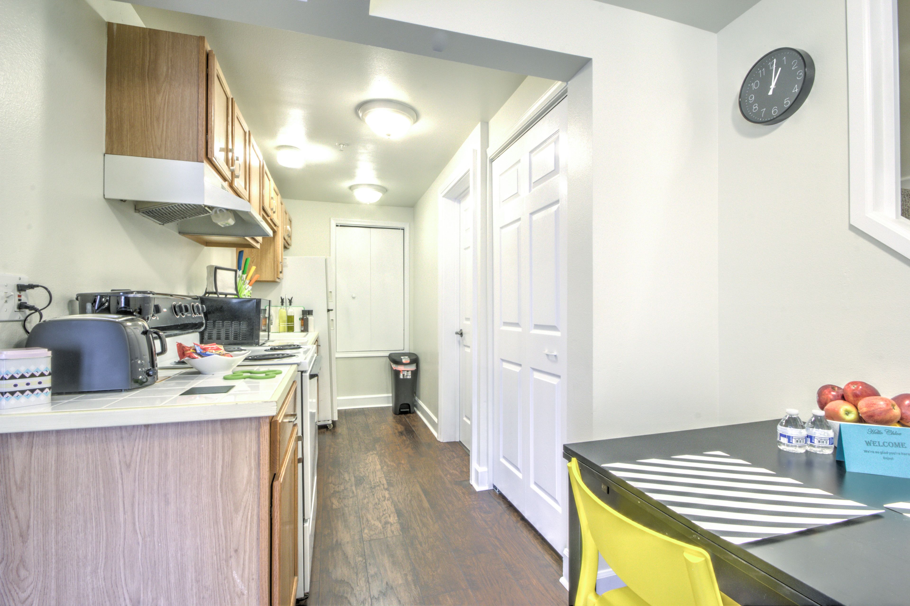 A compact kitchen with wooden cabinets, a toaster, a kettle, and a trash bin.