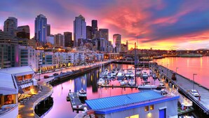A marina with boats docked, a city skyline in the background, and a waterfront restaurant with outdoor seating. - Capitol Hill Apartments (Seattle)