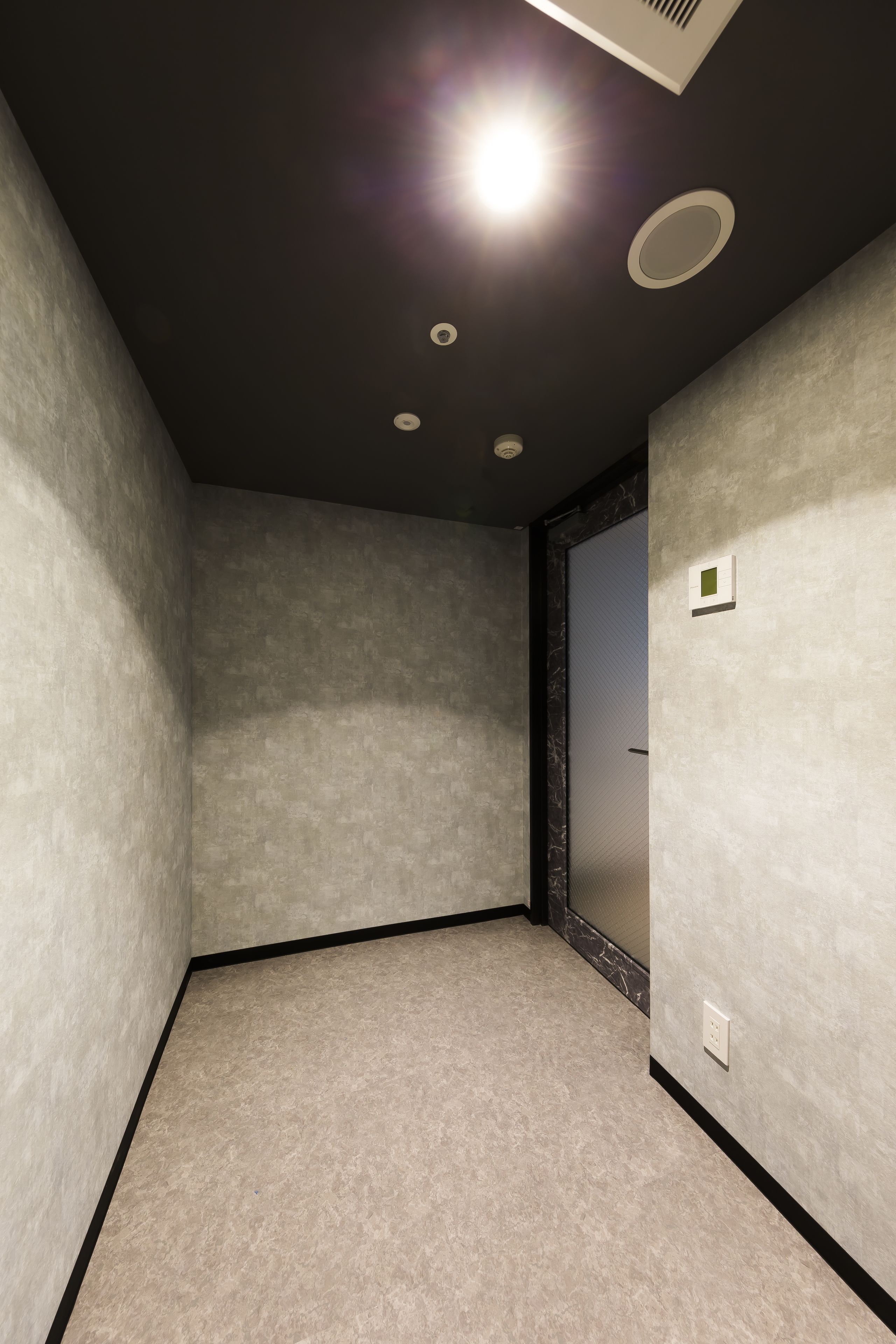 Una habitación con pared texturizada, espejo con marco negro y foco empotrado en el techo.