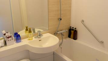 A bathroom with a white sink, mirror, and toilet. There is a showerhead and a grab bar on the wall.