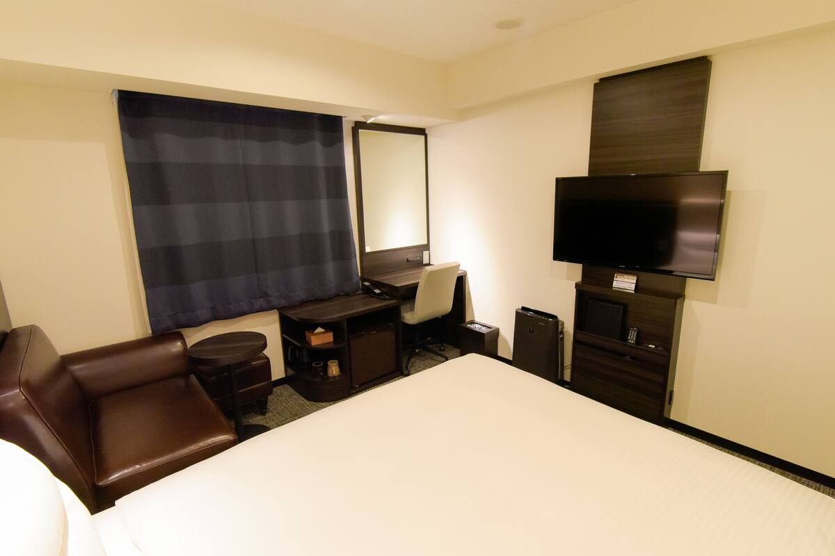 A hotel room with a bed, a desk, a chair, a television, and a large window with a curtain.
