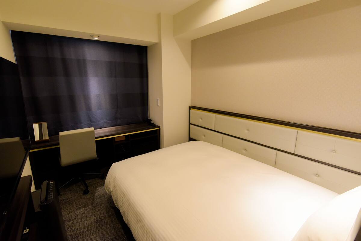 A hotel room with a bed, a desk, a chair, and a window with a curtain.