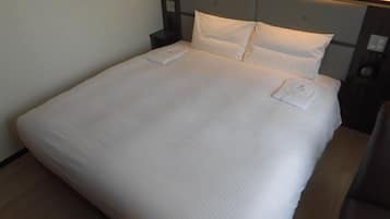 Un lit bien fait, avec du linge de lit blanc, une tête de lit et des tables de chevet dotées de lampes.