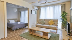 A modern hotel room with a bed, a sofa, a coffee table, and a TV.