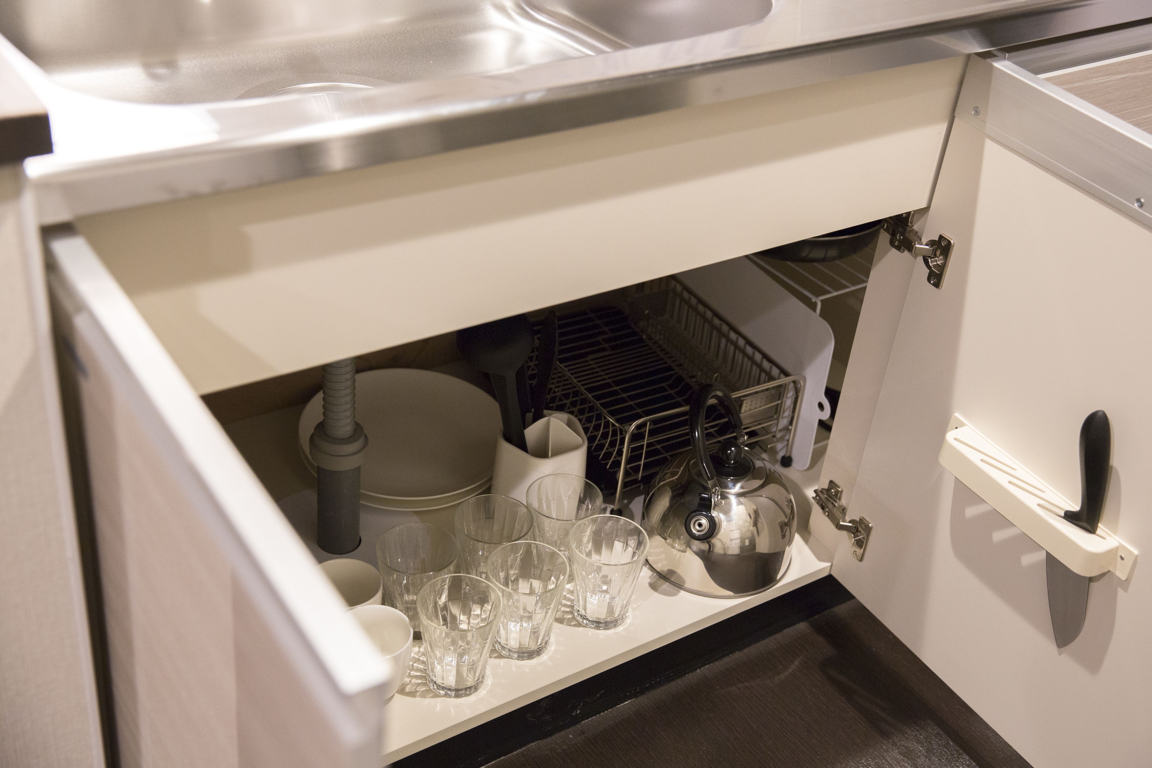 A kitchen with a stainless steel sink, a dish rack, and various kitchen utensils.
