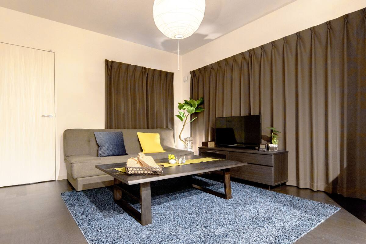 Una sala de estar moderna con un sofá, una mesa de centro, un televisor y cortinas.