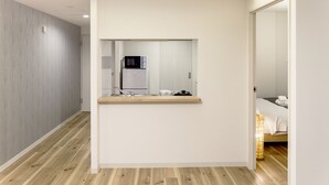 A modern hotel room with a wooden floor, a small kitchenette, a bed, and a bathroom visible through an open door.