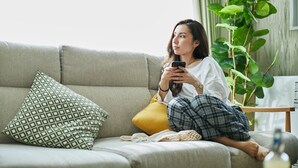 A person sitting on a sofa with a smartphone, a patterned pillow, and a yellow cushion.