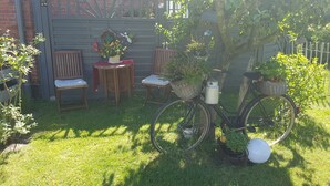 A garden with a wooden table and chairs, a bicycle with baskets, and a brick wall. - Cozy apartment with maritime charm (Langenhorn)