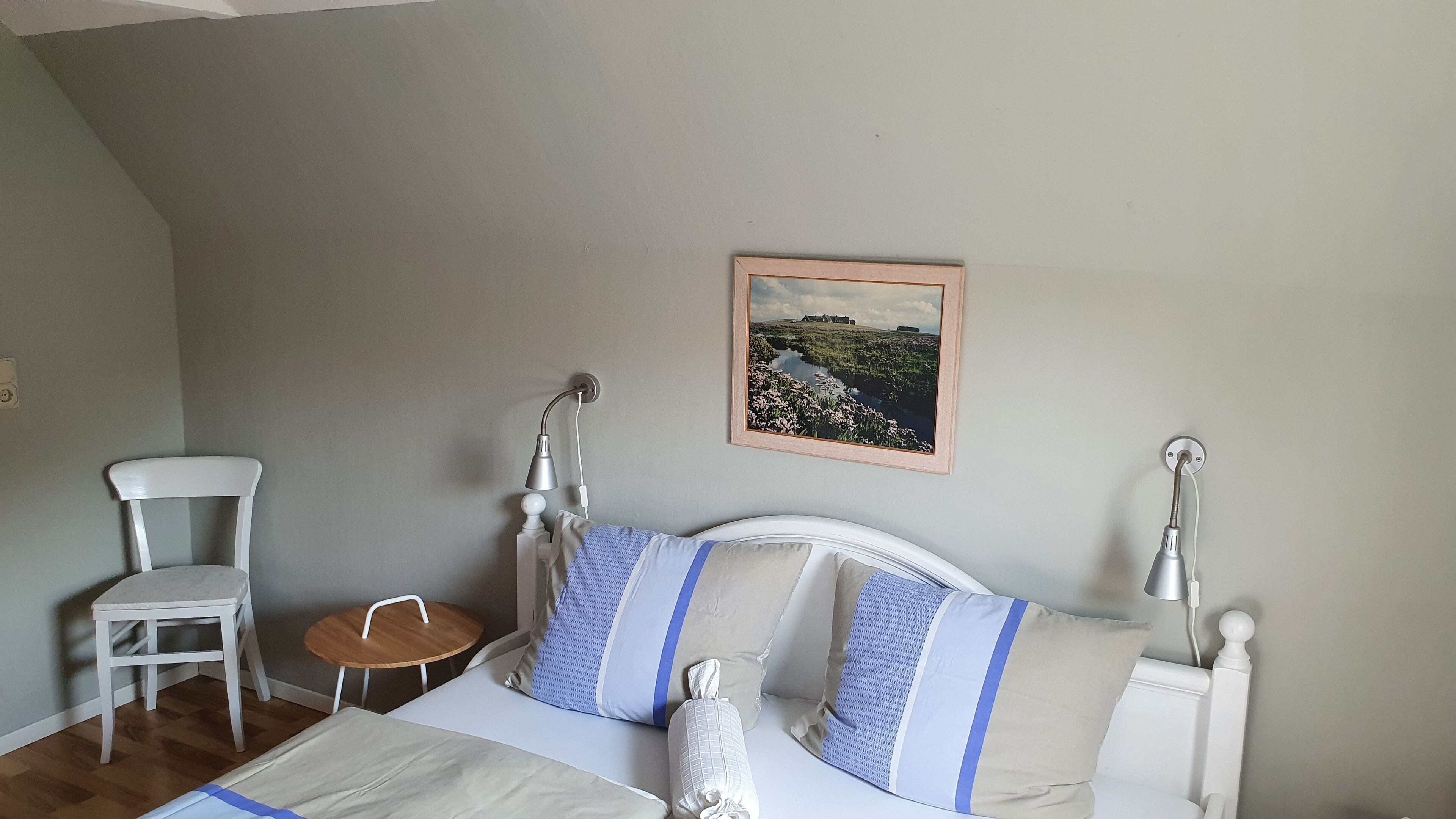 Une chambre à coucher avec un lit, une chaise, une petite table et un tableau au mur.