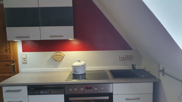 A compact kitchen with a stove, sink, and a dish rack.