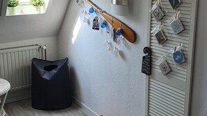 A cozy attic room with a sloped ceiling, a small window with a view of greenery, a wooden beam, and a collection of decorative items including a hat, a book, and various ornaments. - Cozy apartment with maritime charm (Langenhorn)