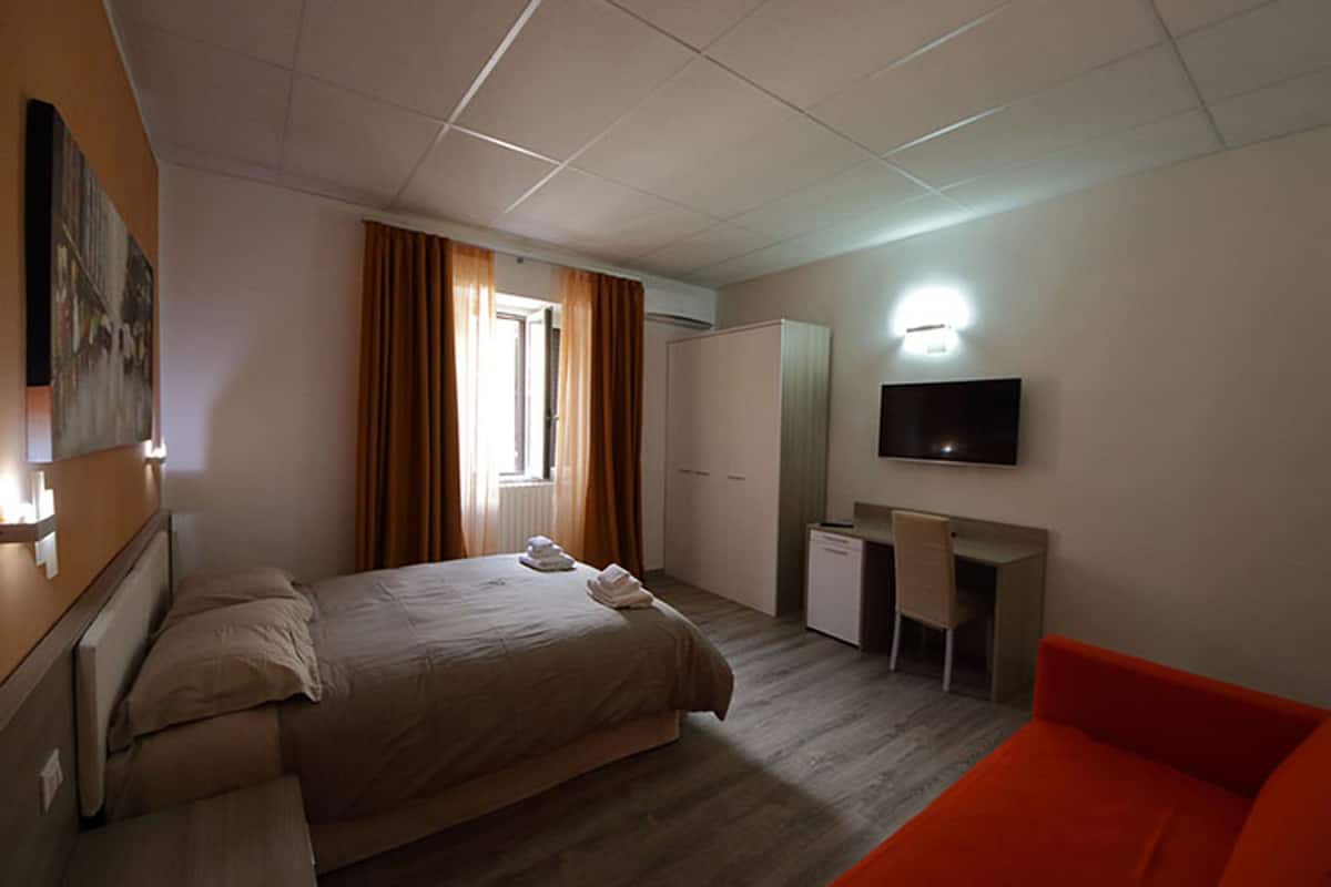 Una habitación de hotel con una cama, un escritorio, un televisor y un sofá rojo.