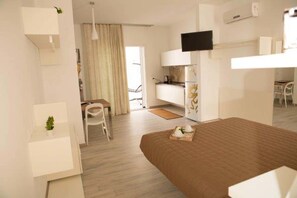 A modern hotel room with a bed, a desk, a chair, a TV, and a kitchenette. - Nidi di Feo (Lecce)