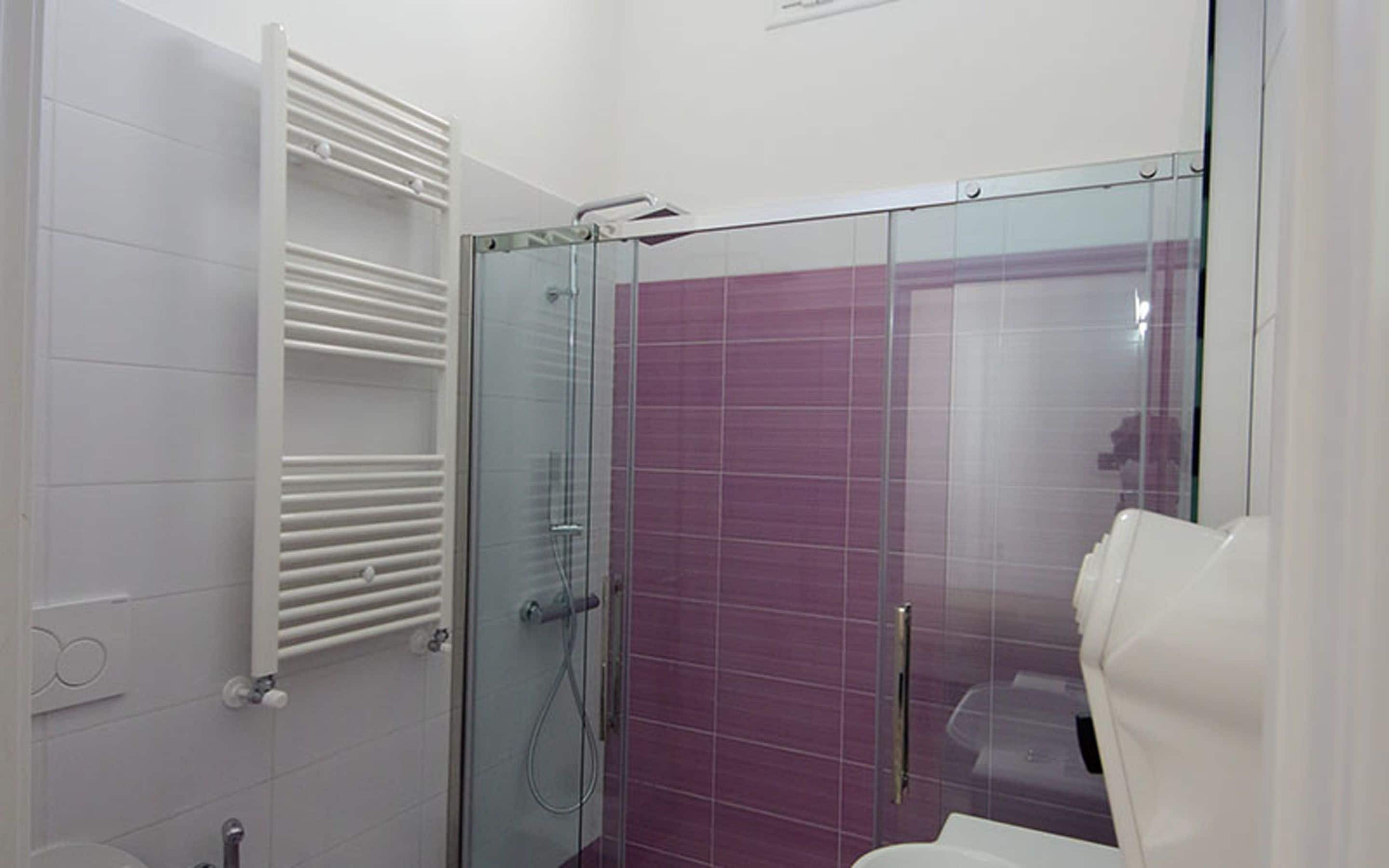 Ein modernes Badezimmer mit Duschkabine aus Glas, weiß geflieste Wände und einer weißen Toilette.