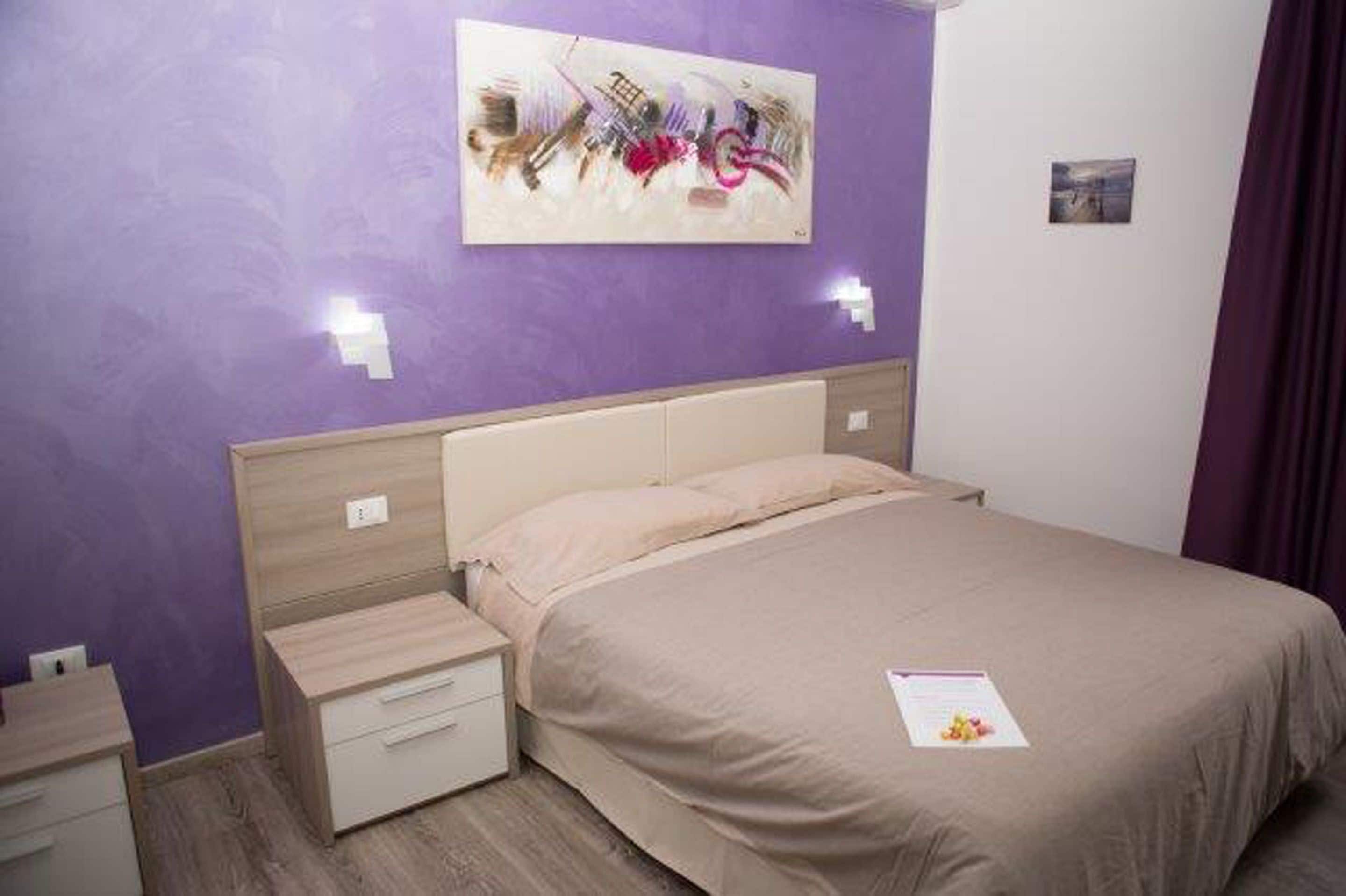 Une chambre à coucher comprenant un lit, une table de chevet, un tiroir, une lampe fixée au mur et un tableau.