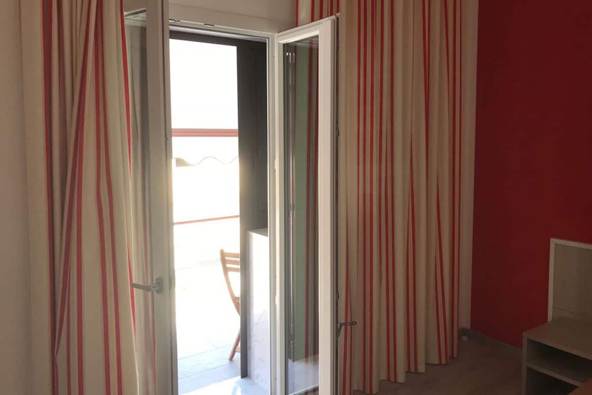 Una habitación con puerta de vidrio corrediza que da a un espacio exterior, pared roja y una pequeña mesa.